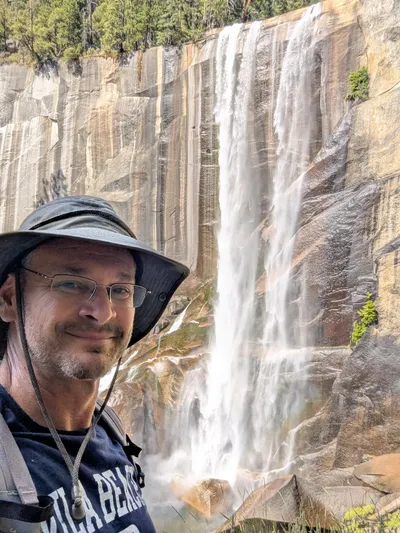 Mike at a waterfall in a sun hat and Vila Beach shirt